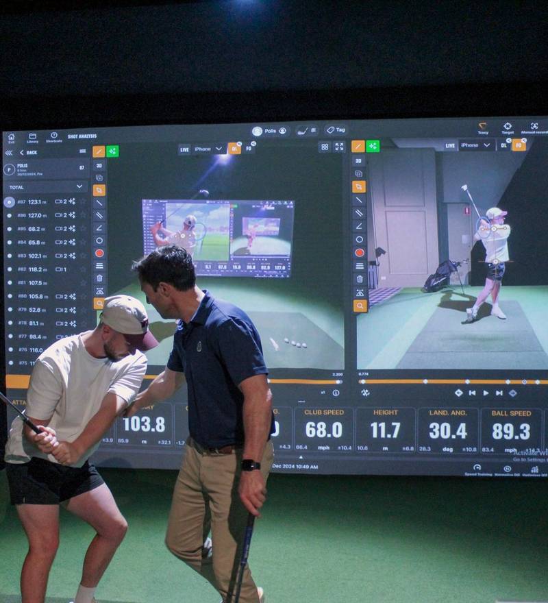 A host giving a guest a quick swing tip in front of the TrackMan data screen