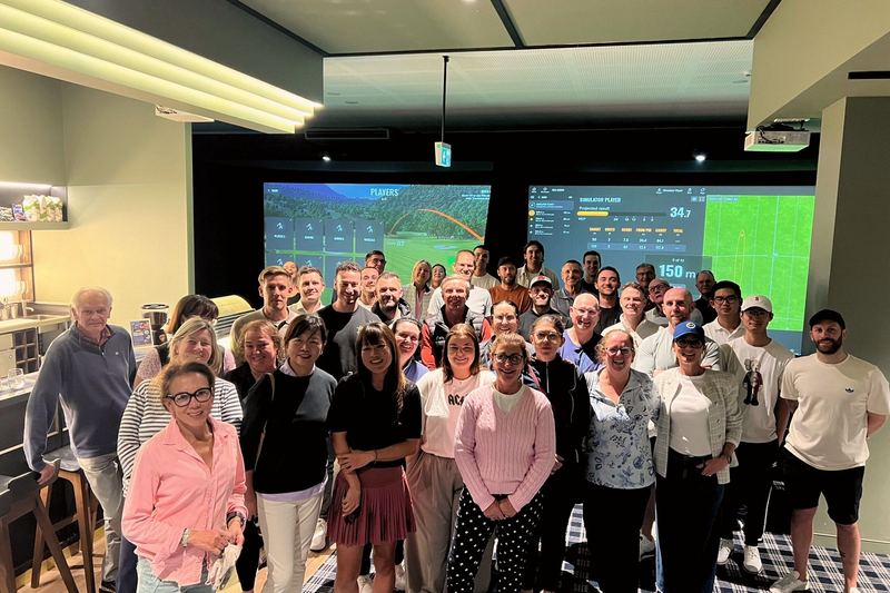A large corporate group together in front of the TrackMan screens at Howe2Golf