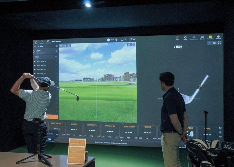 A guest mid-swing on a TrackMan bay while the host watches